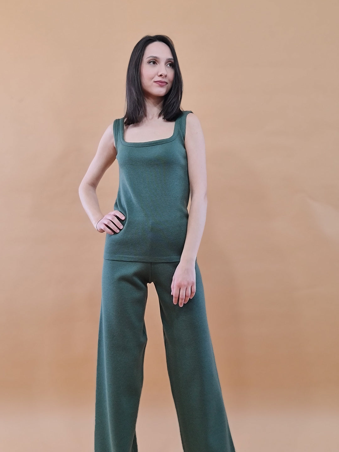 Confident woman in green sleeveless top and wide-leg pants against beige background