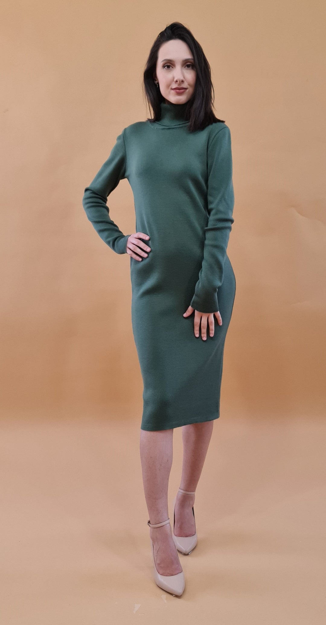 Woman in green turtleneck dress posing against beige background