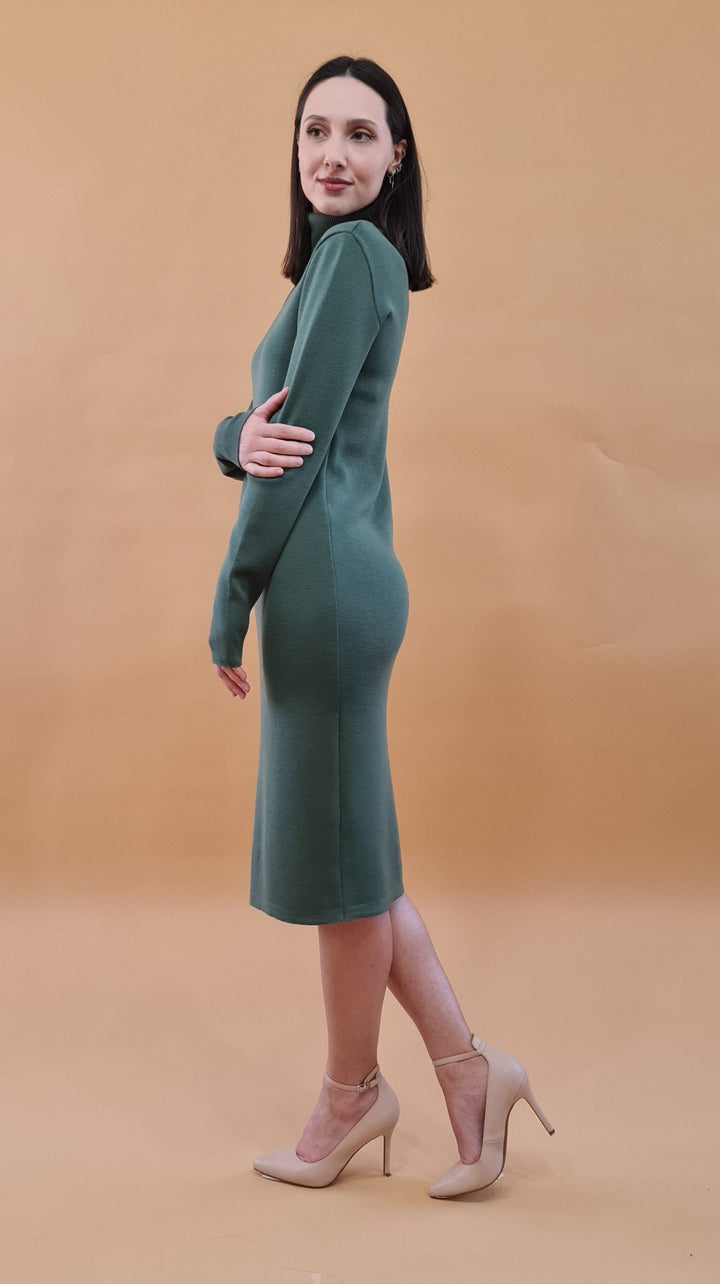 Woman wearing a green long-sleeve dress and beige high heels against a beige background