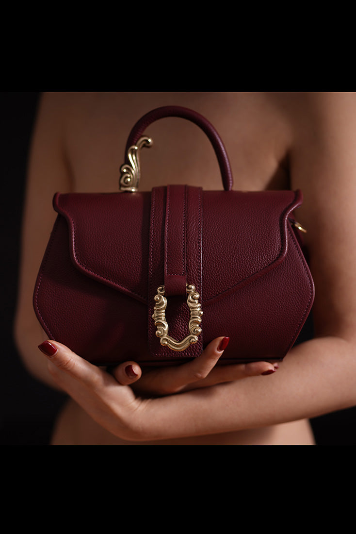 Elegant woman holding a burgundy leather handbag with gold accents
