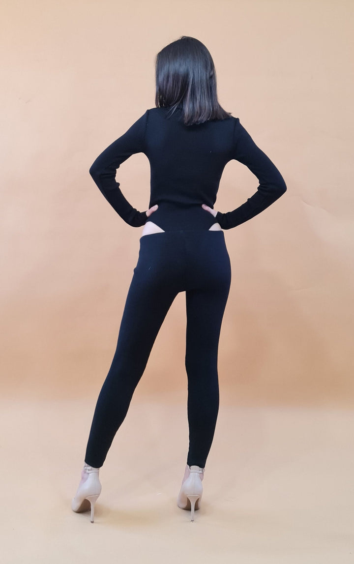 Person wearing a black outfit with high heels standing against a beige background, facing away