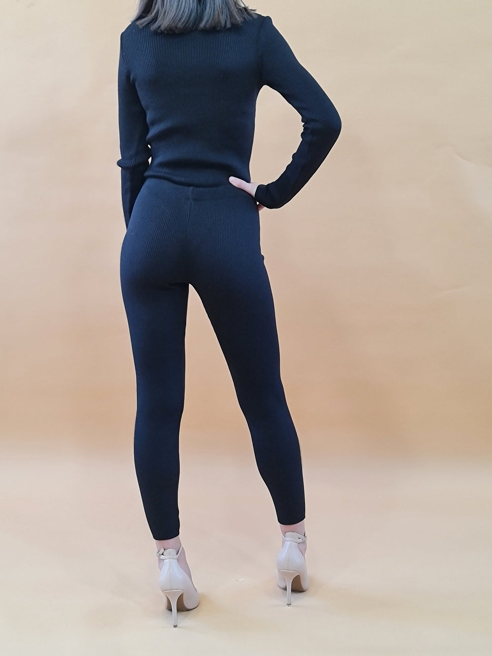 Woman in a black sweater and leggings posing against a beige background