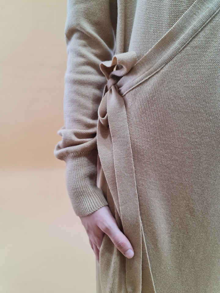 Close-up of a person wearing a beige knit cardigan with a bow detail