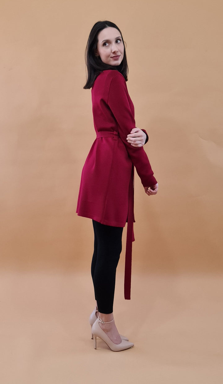 Woman in red coat and black leggings posing against a beige background