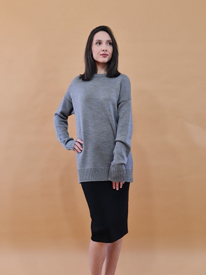 Woman posing in casual grey sweater and black skirt with beige background