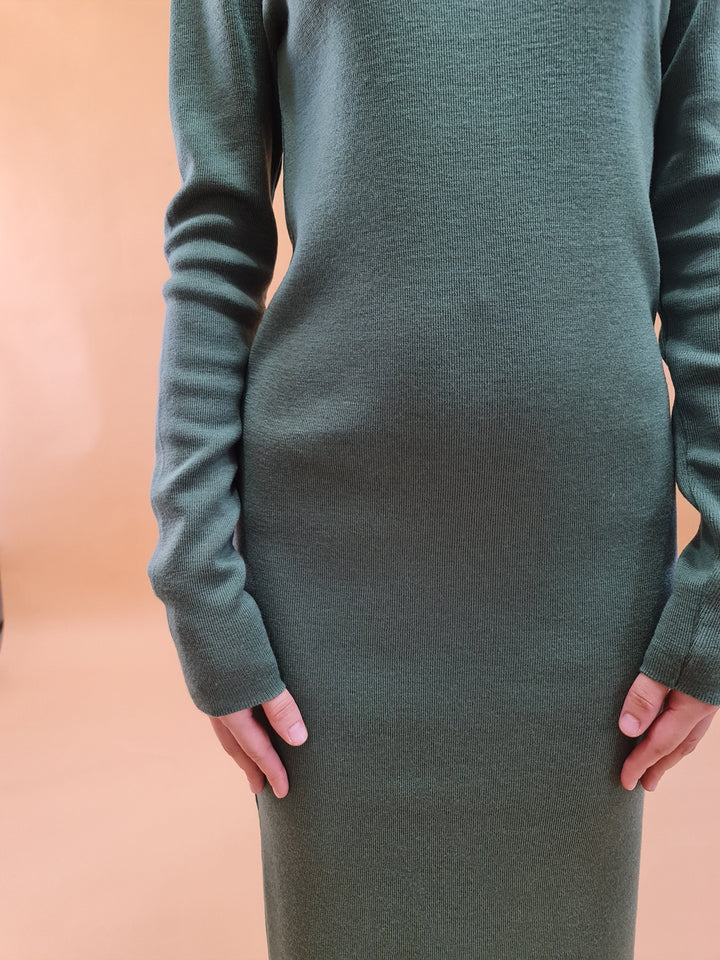 Person wearing a green long-sleeve knit dress on a beige background