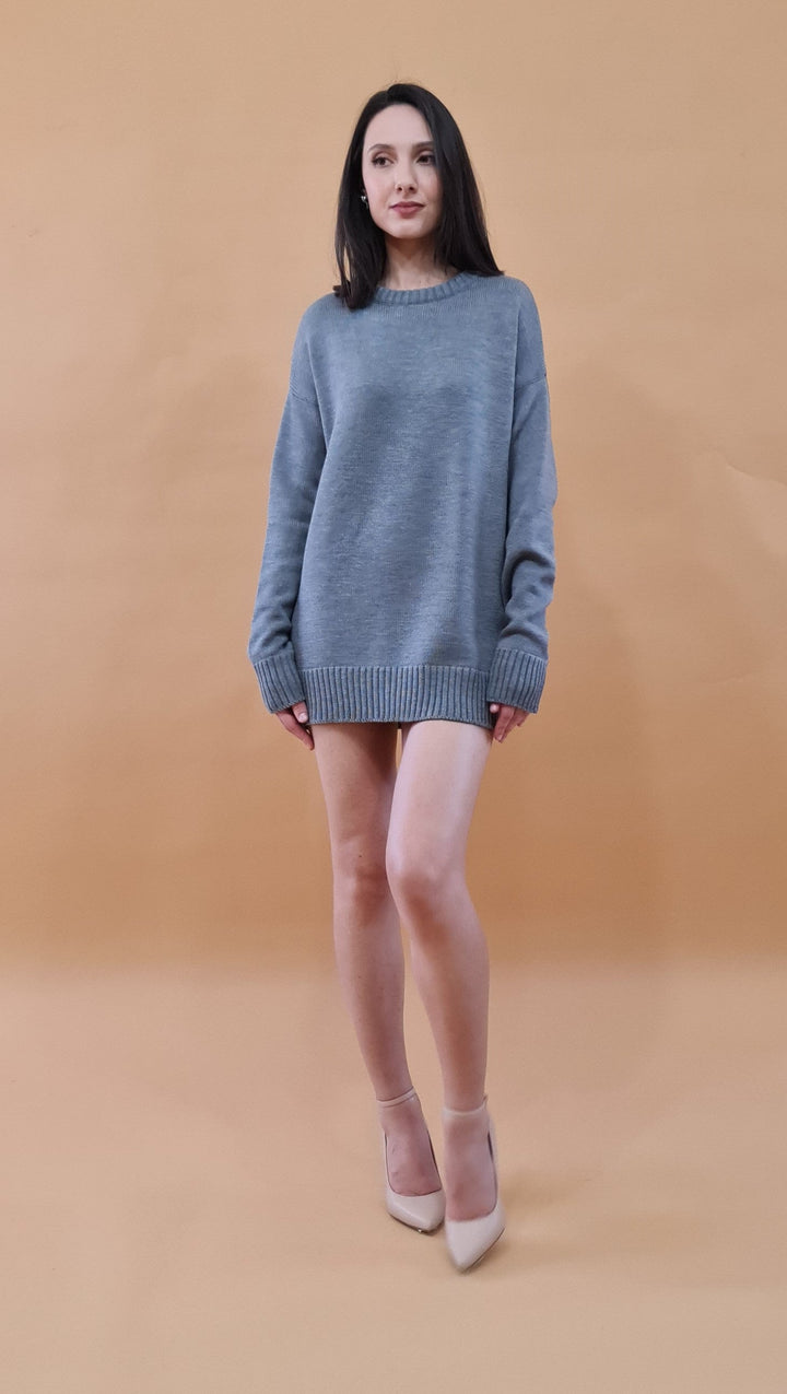 Woman wearing oversized gray sweater and beige heels against a beige background