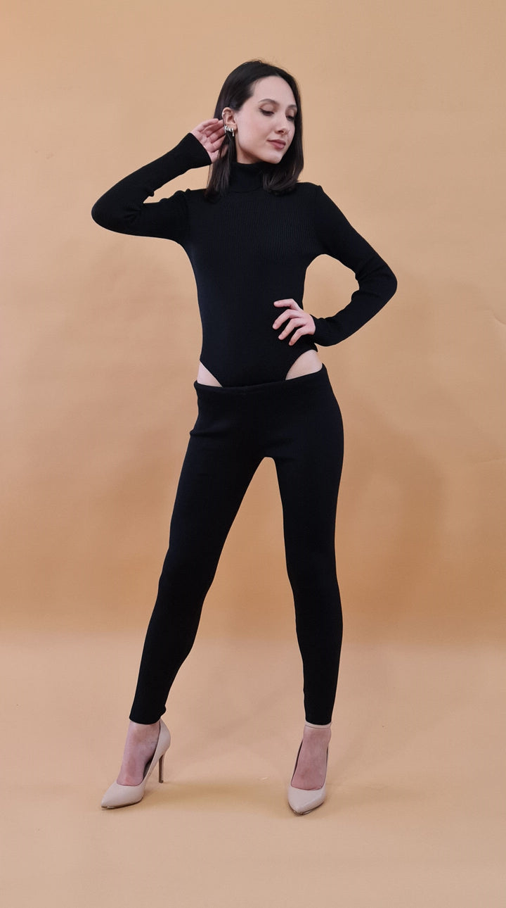 Woman wearing a stylish black outfit with cut-out leggings and beige heels against a beige background