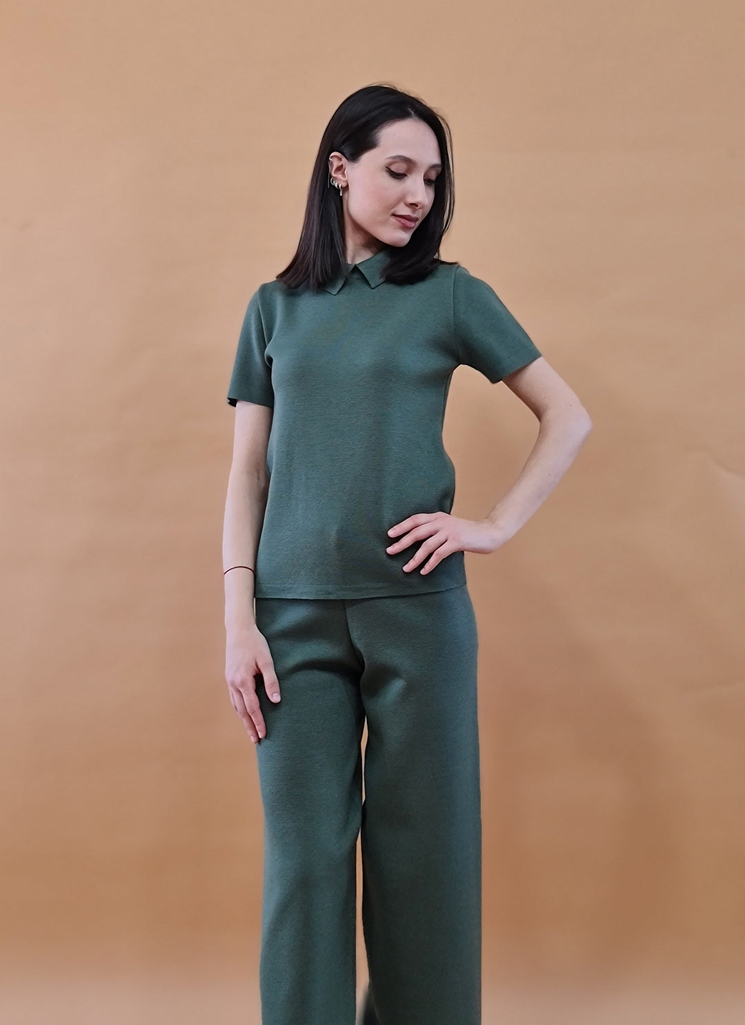 Woman wearing green collared short-sleeve shirt and matching wide-leg pants set against a tan background