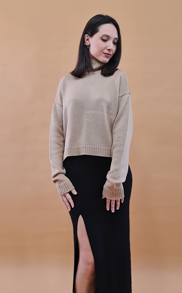 Woman in beige sweater and black skirt with a high slit against a brown background