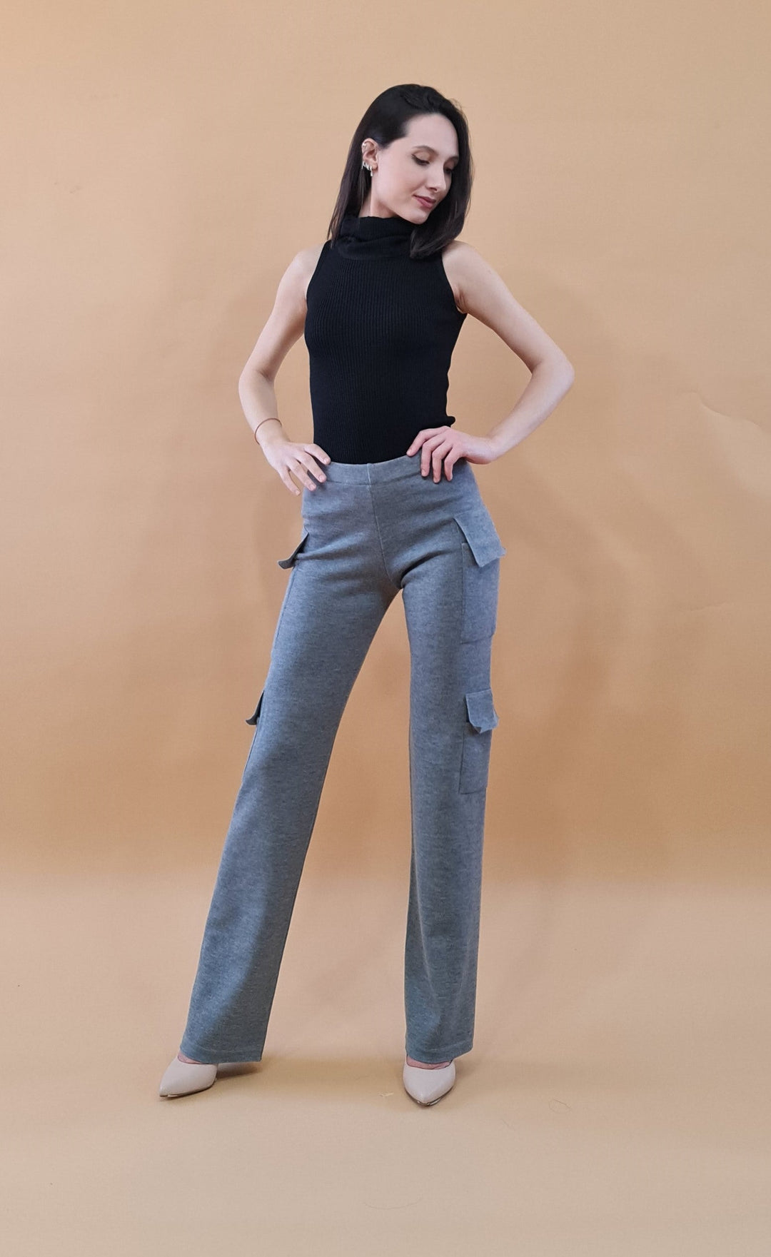 Woman modeling black sleeveless top and gray cargo pants against beige background