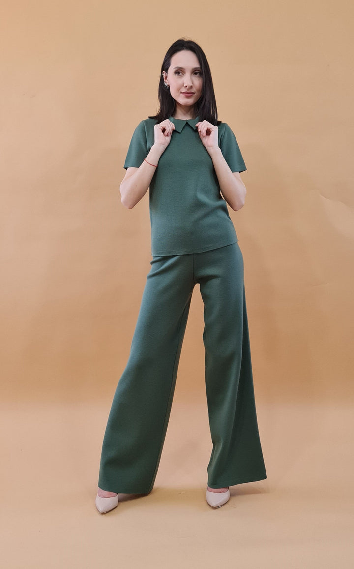 Woman wearing a green matching trouser set posing against a tan background
