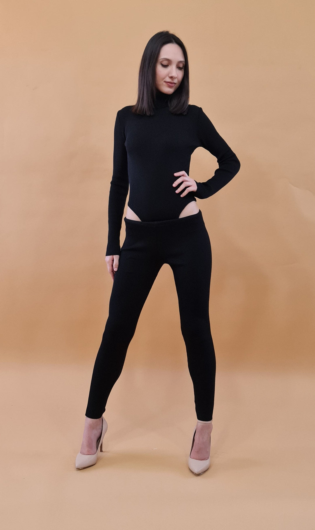 Woman in black fitted outfit posing against beige background