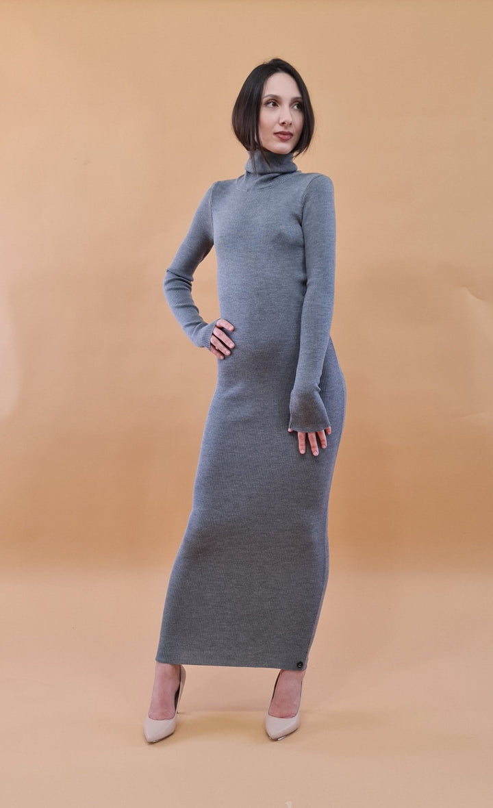 Woman posing in a long gray sweater dress against a beige background