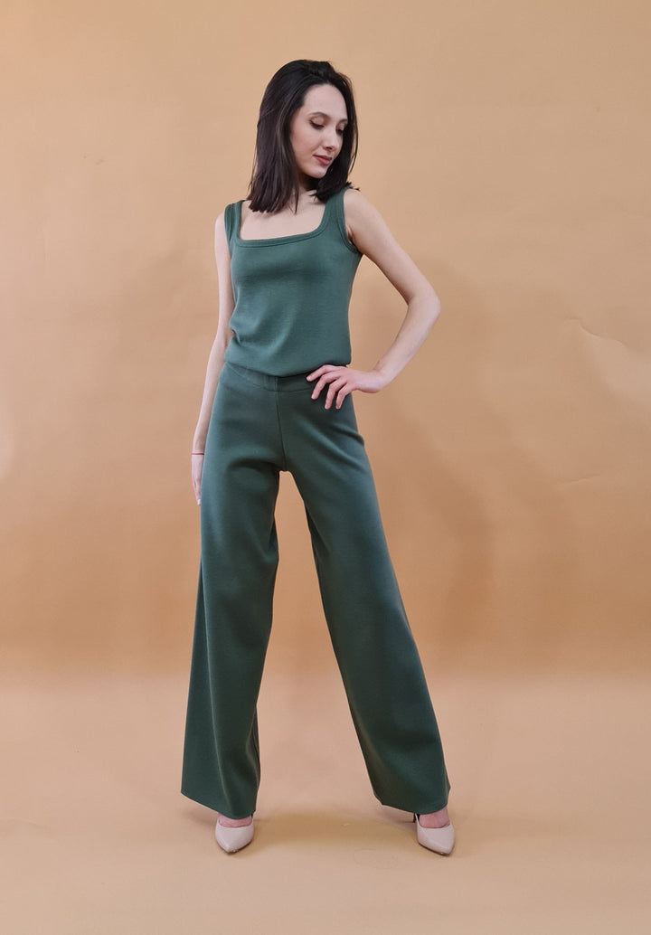 Woman wearing a stylish green jumpsuit posing confidently against a beige background