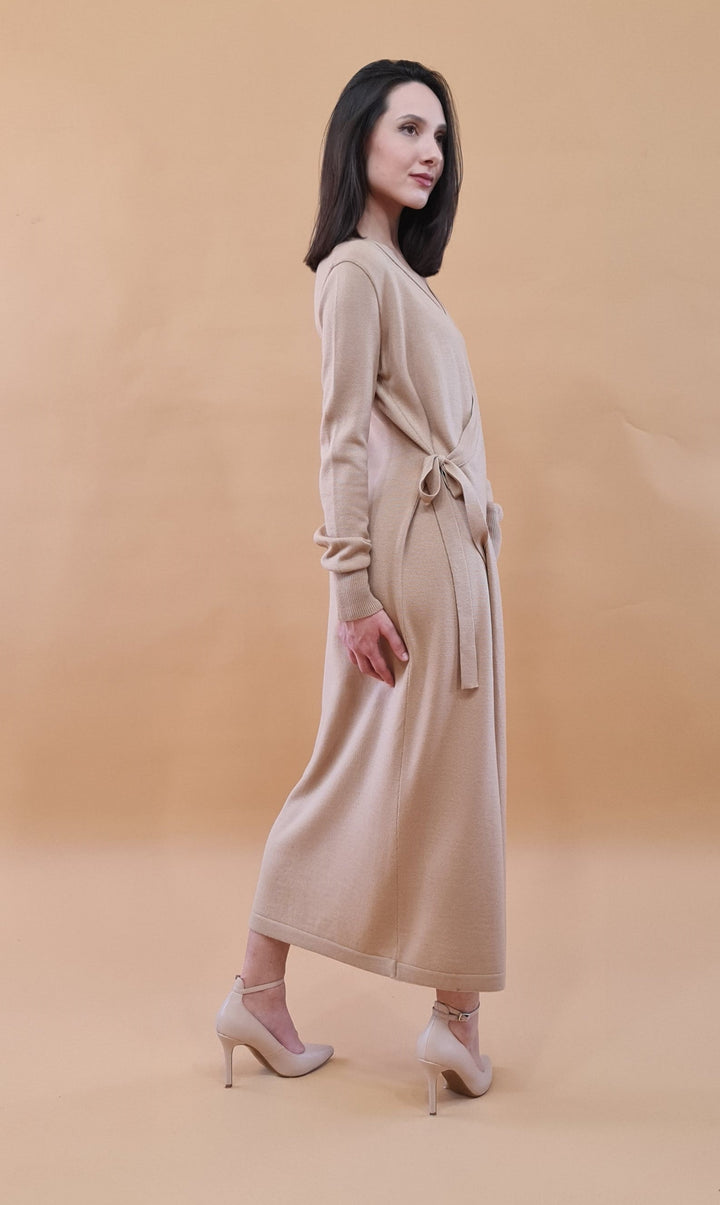 Woman in a beige long-sleeve wrap dress and high heels against a tan background