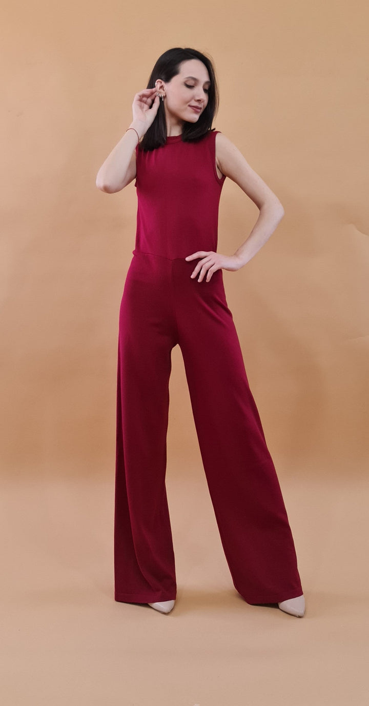 Woman wearing a stylish red jumpsuit posing confidently against a beige background