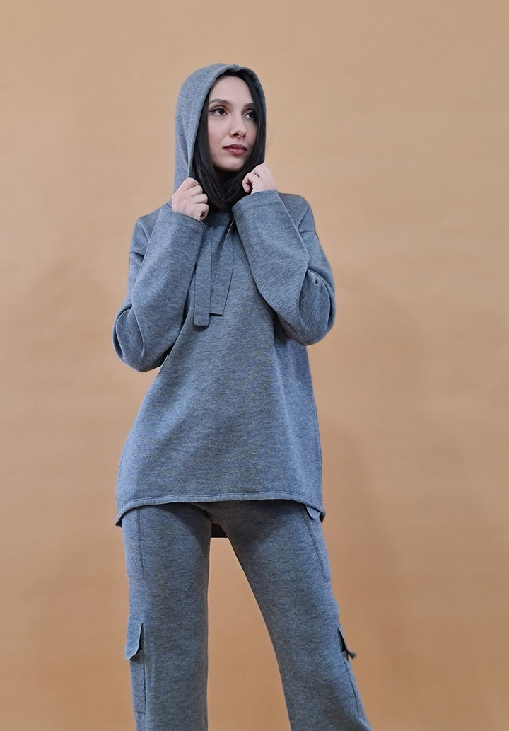 Woman wearing a gray hooded sweatshirt and matching pants against a beige background