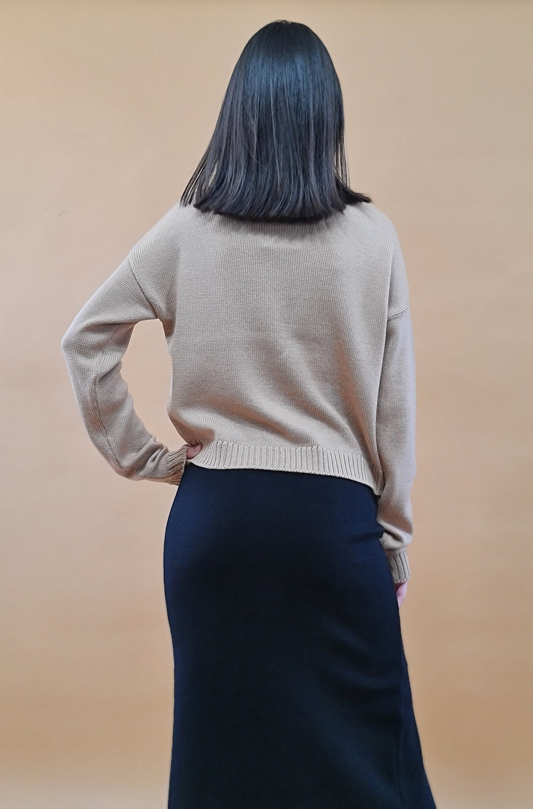 Woman with medium-length black hair facing away, wearing a beige knit sweater and black skirt