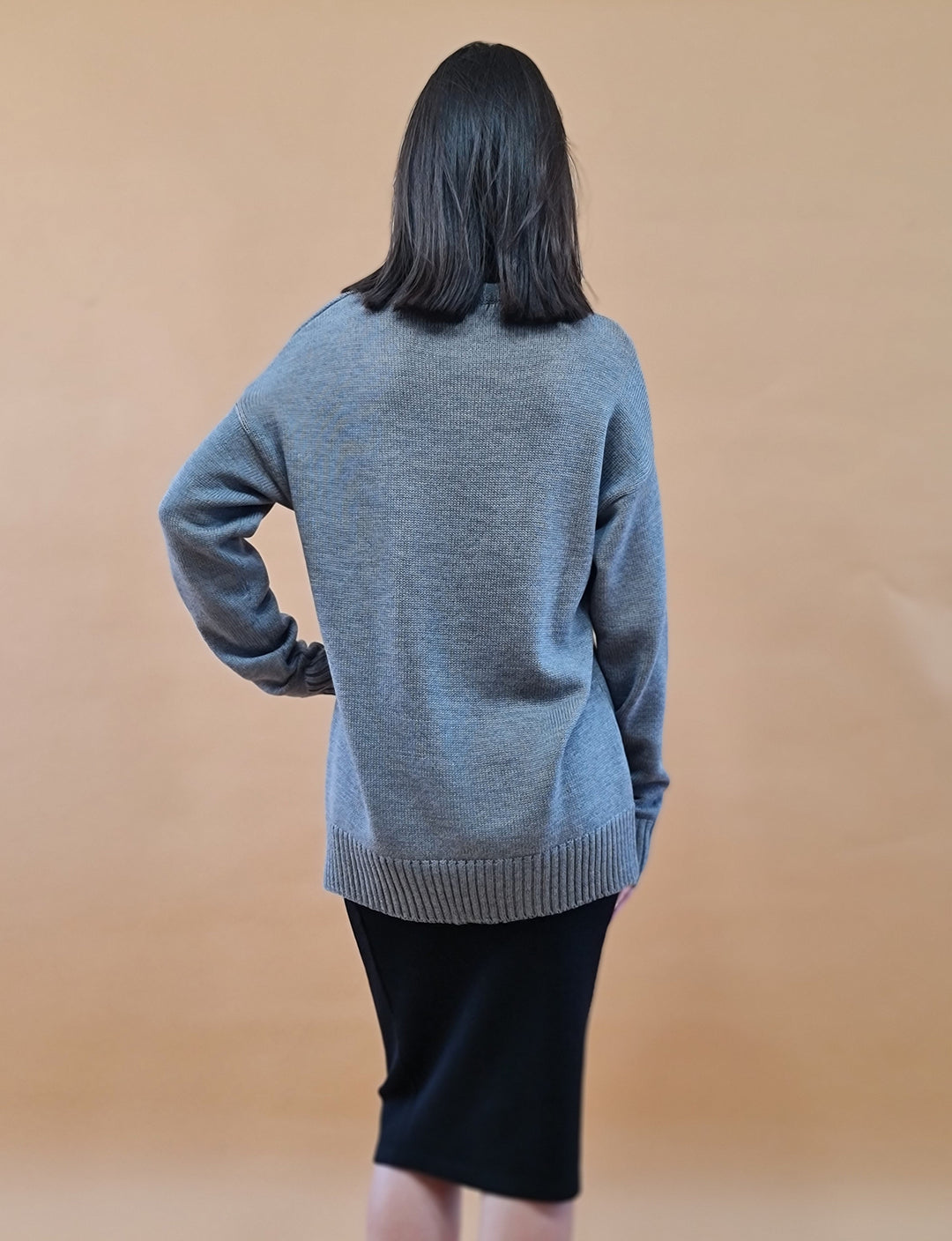 Back view of a woman wearing a gray sweater and black skirt against a beige background