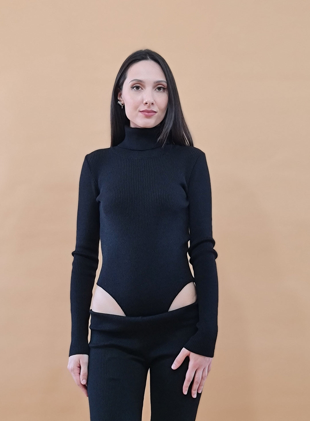 Woman wearing black turtleneck cut-out sweater against tan background