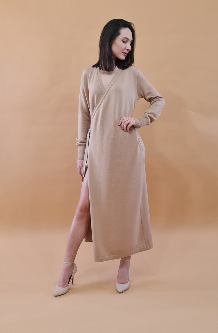 Woman modeling beige wrap dress with side slit and high heels against a tan background