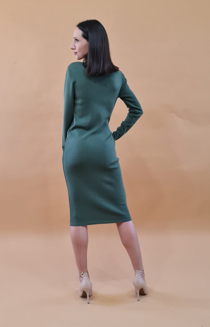 Woman in green dress and high heels standing against a beige background