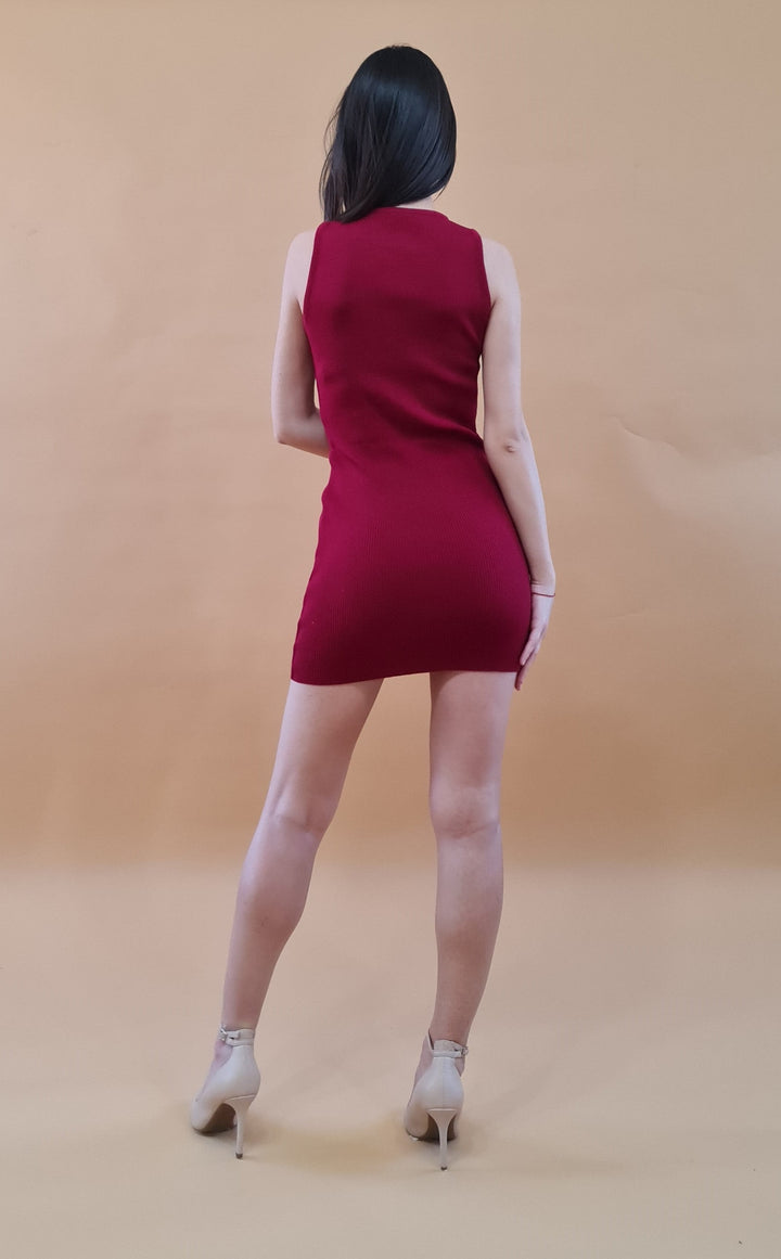 Woman in red sleeveless dress and high heels facing backwards against beige background