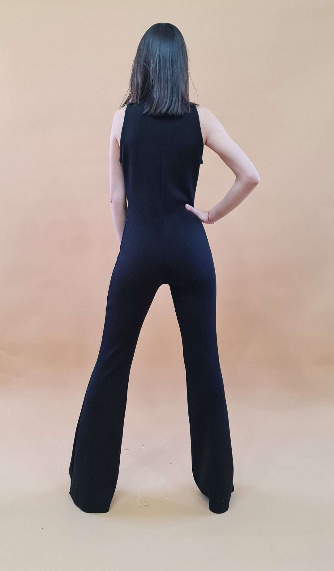 Woman in stylish black jumpsuit with back to camera against beige background