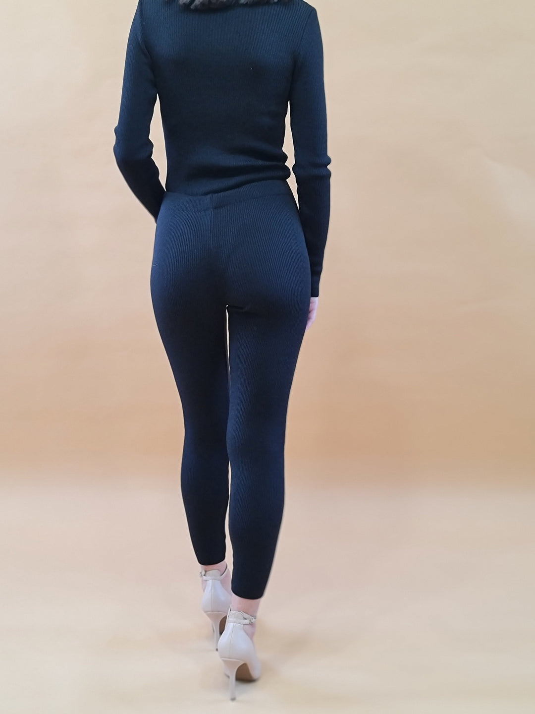 Back view of a woman wearing black ribbed knit sweater and pants set with high heels