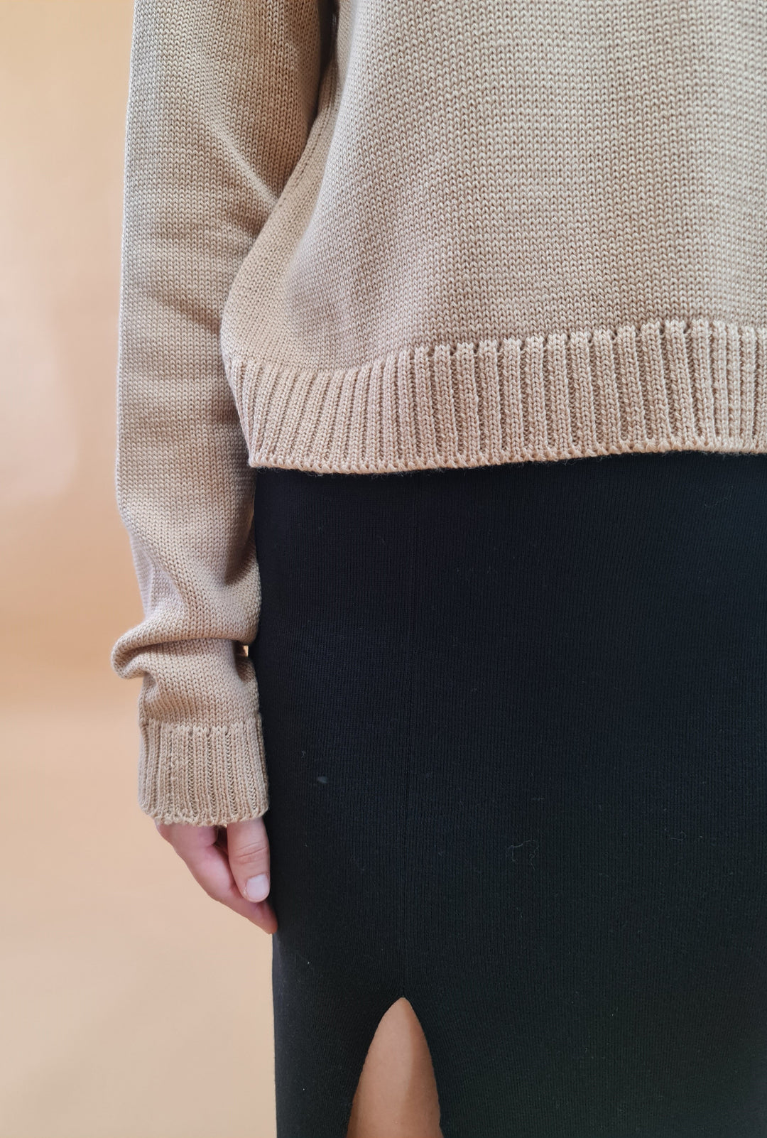 Close-up of woman wearing beige knit sweater and black skirt with side slit
