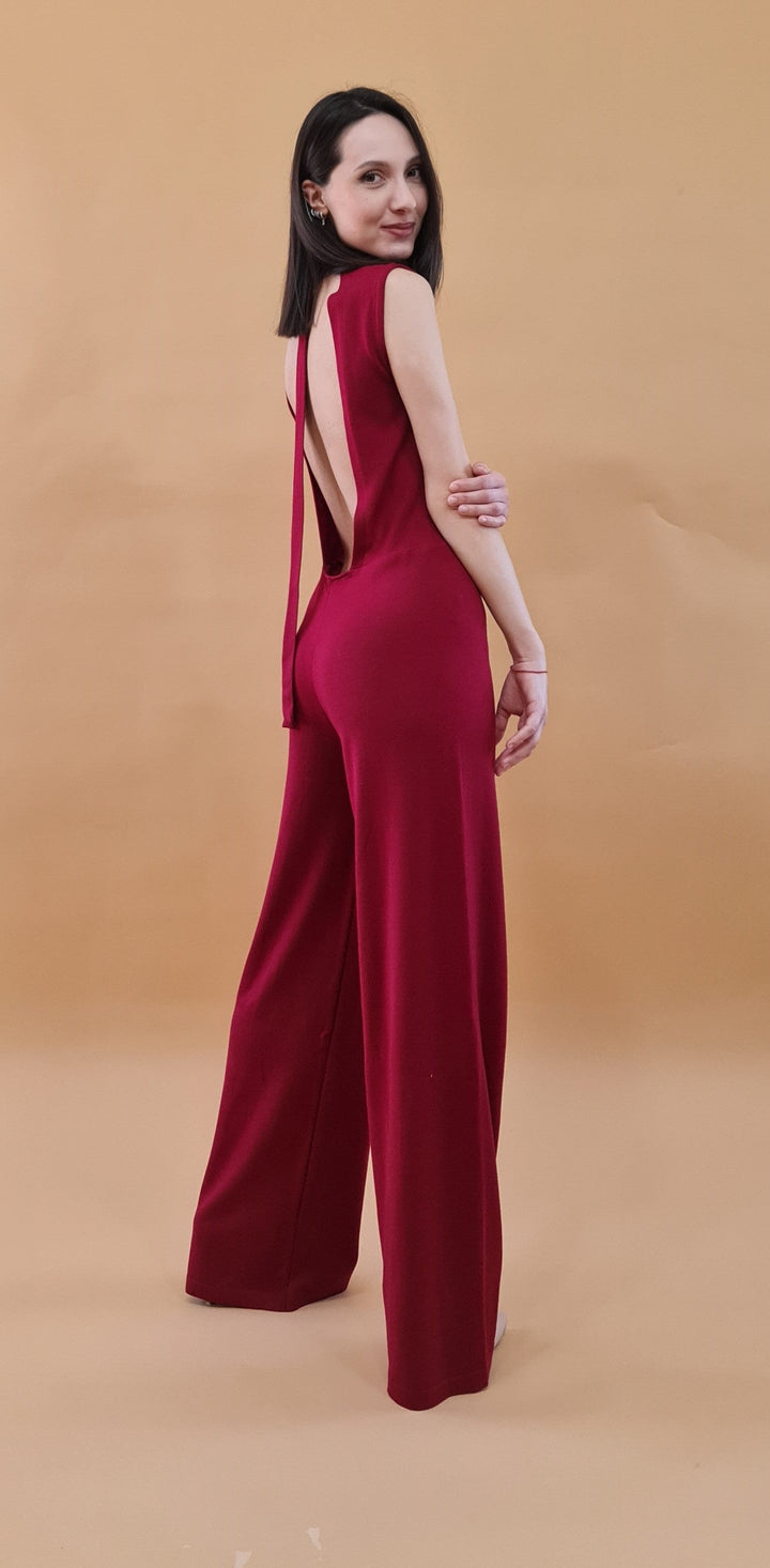 woman wearing backless red jumpsuit on beige background