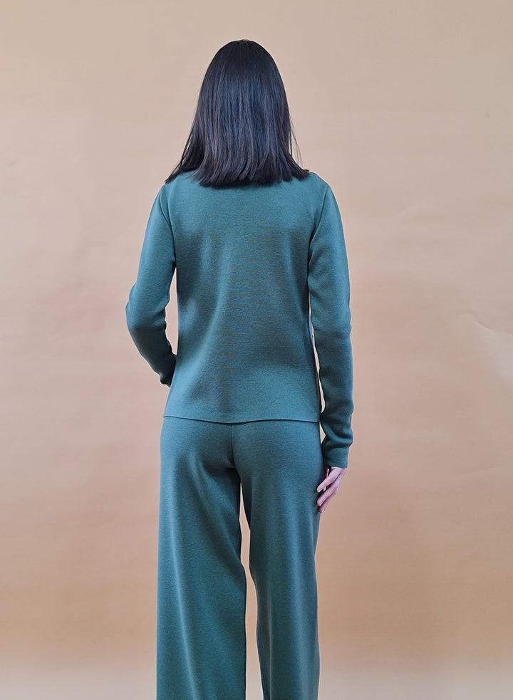 Person wearing a green sweater and pants set, facing backward against a beige background