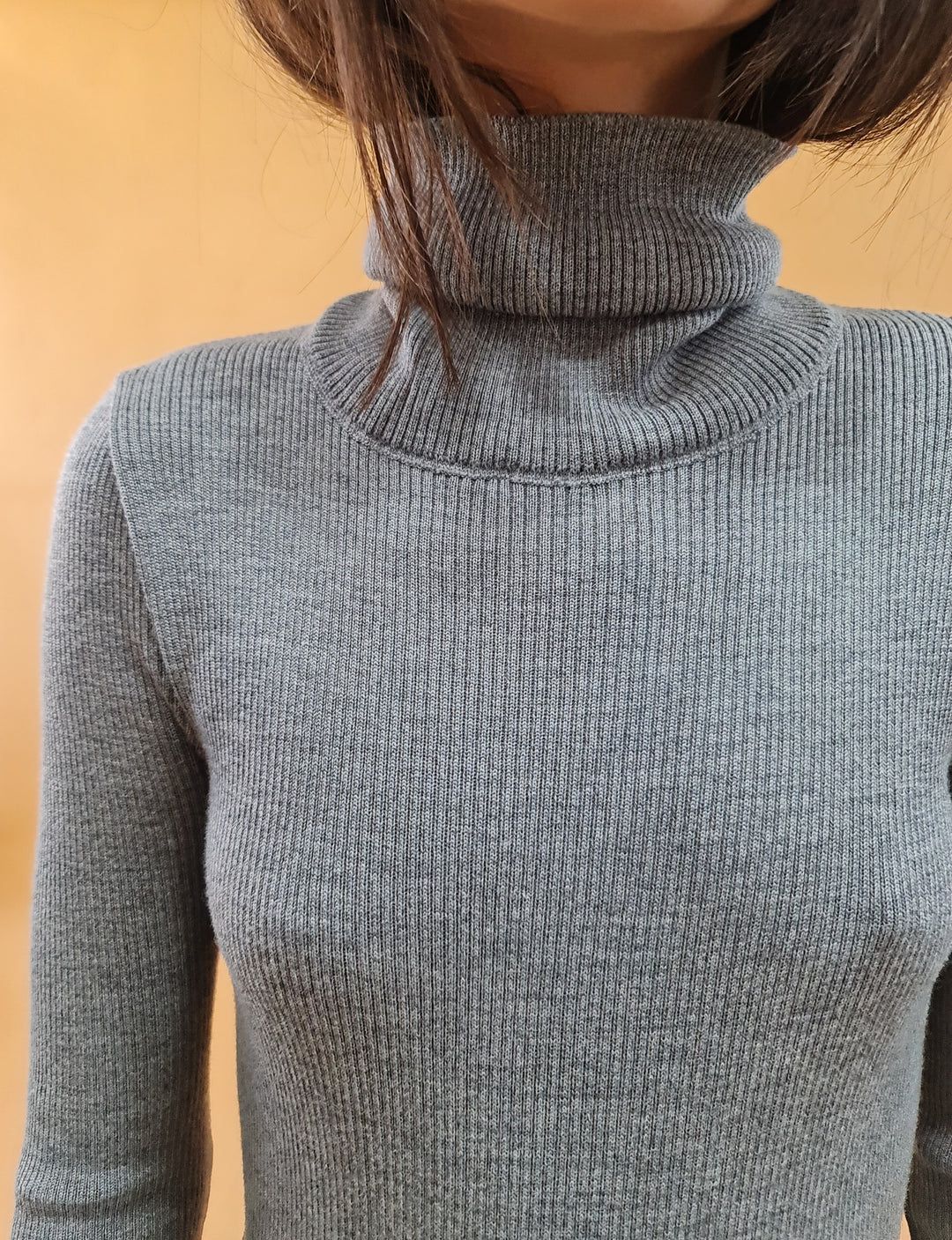 Gray ribbed turtleneck sweater on person against orange background