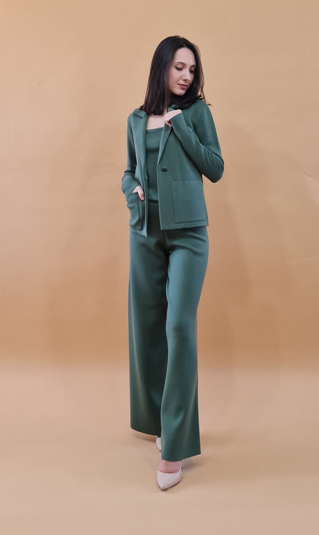 Woman wearing green suit with matching blazer and wide-leg pants on beige background