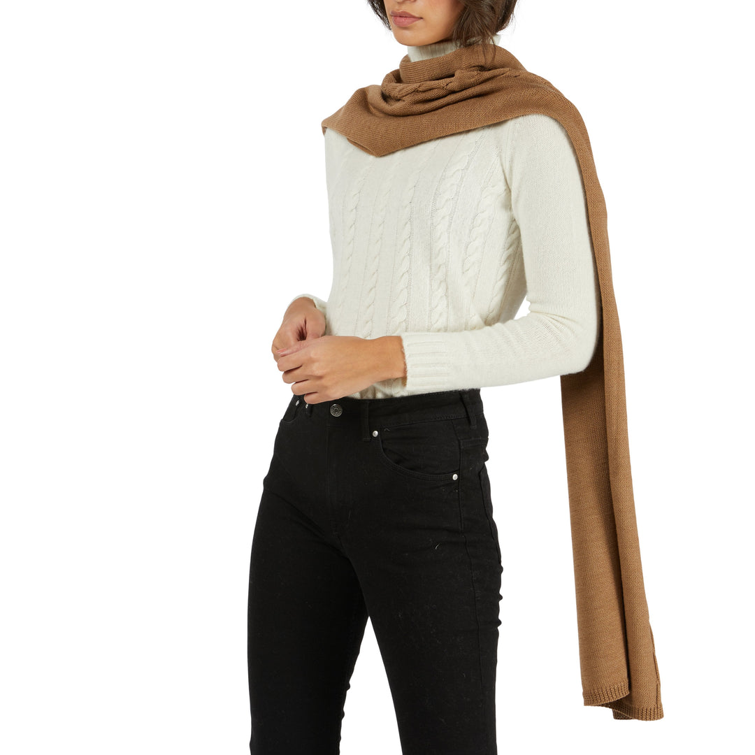 Woman wearing a white cable knit sweater, black pants, and brown scarf