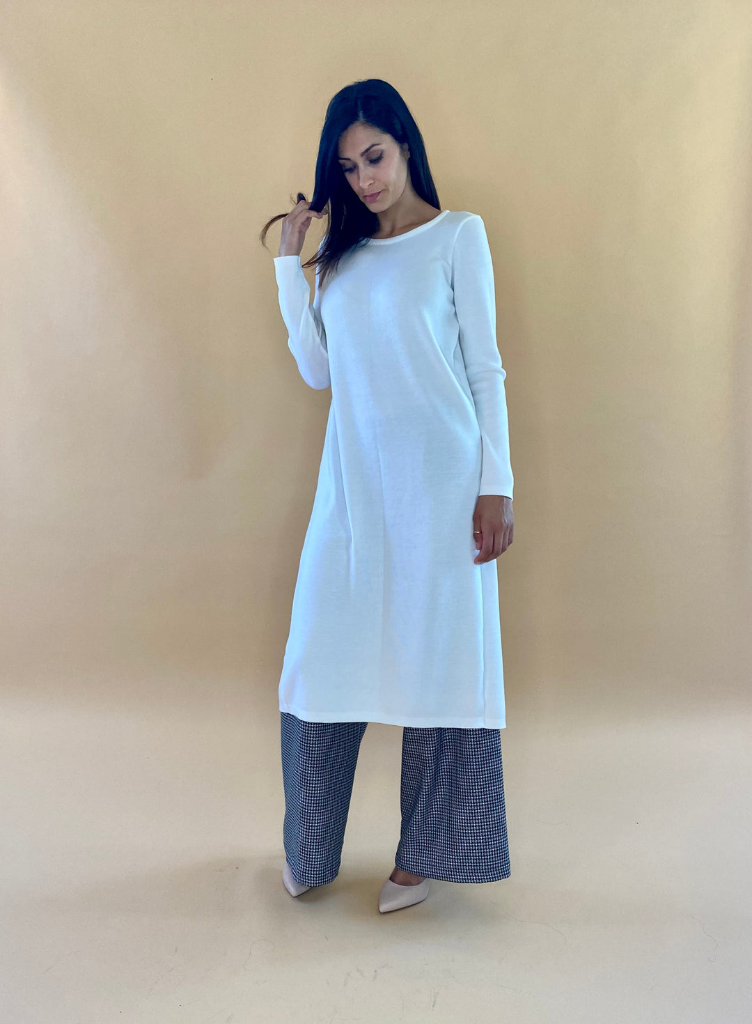 Woman wearing a long white tunic with gray wide-leg pants against a beige background