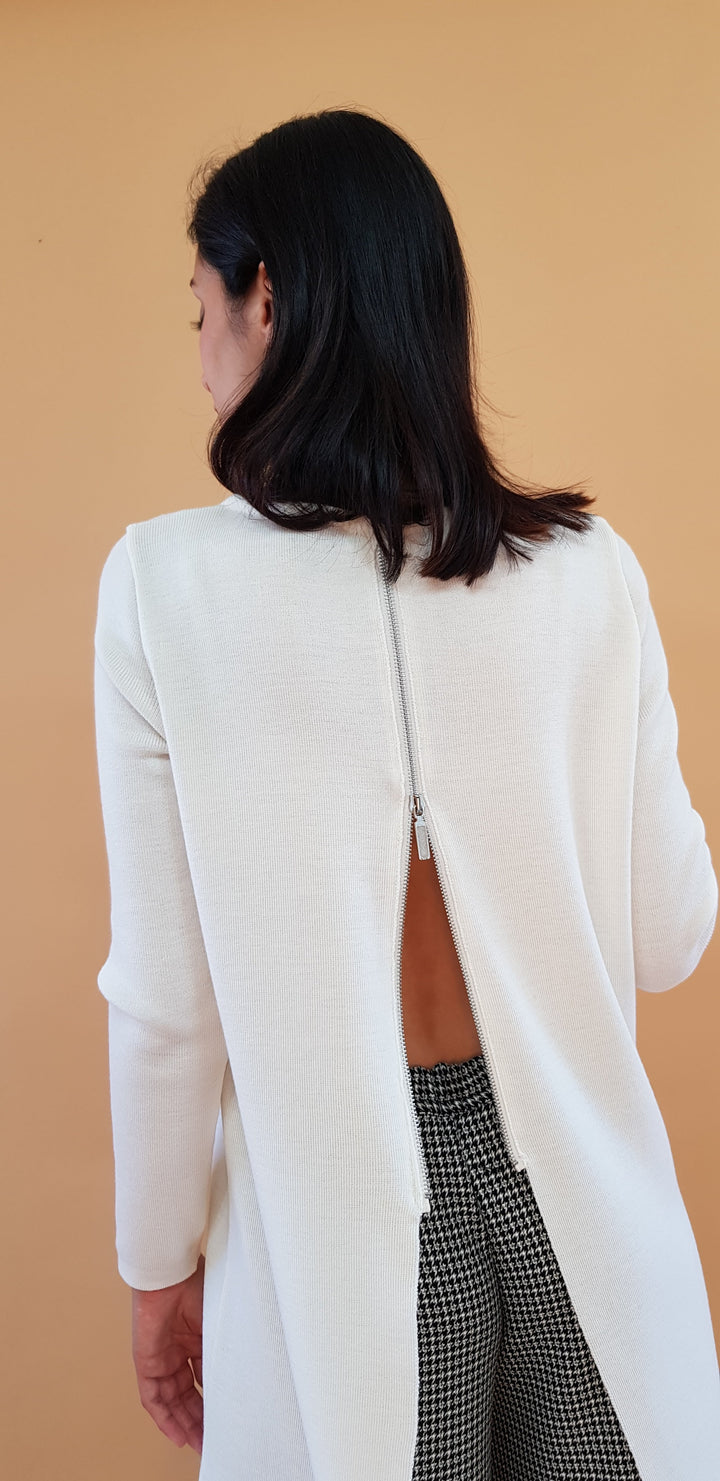 Woman wearing a white open-back sweater with black hair styled simply against a beige background