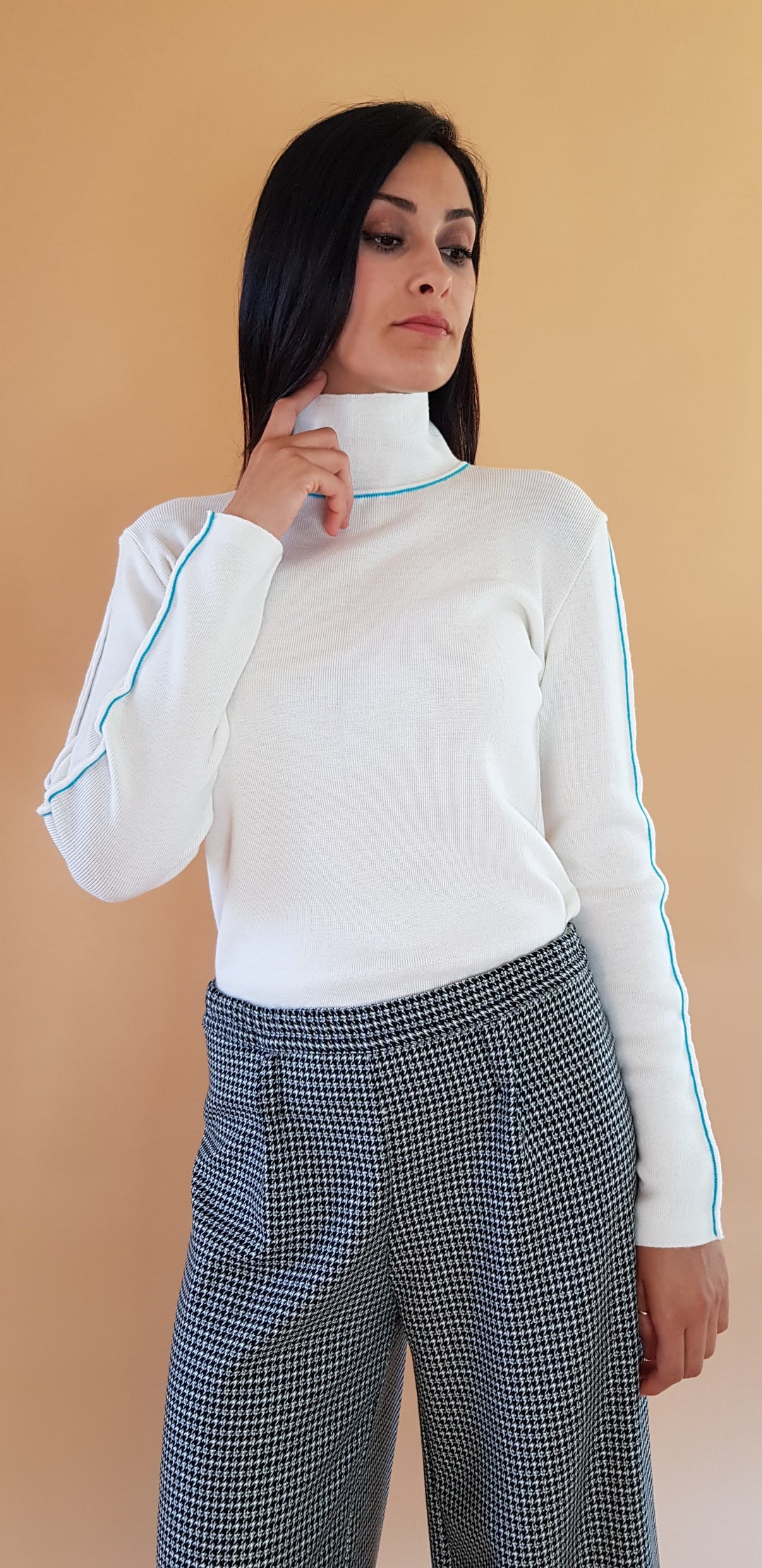 Woman wearing a white turtleneck sweater and houndstooth pants against a beige background