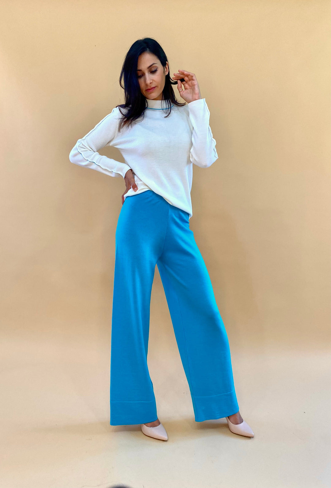 Woman modeling white long-sleeve top with blue wide-leg pants against beige background