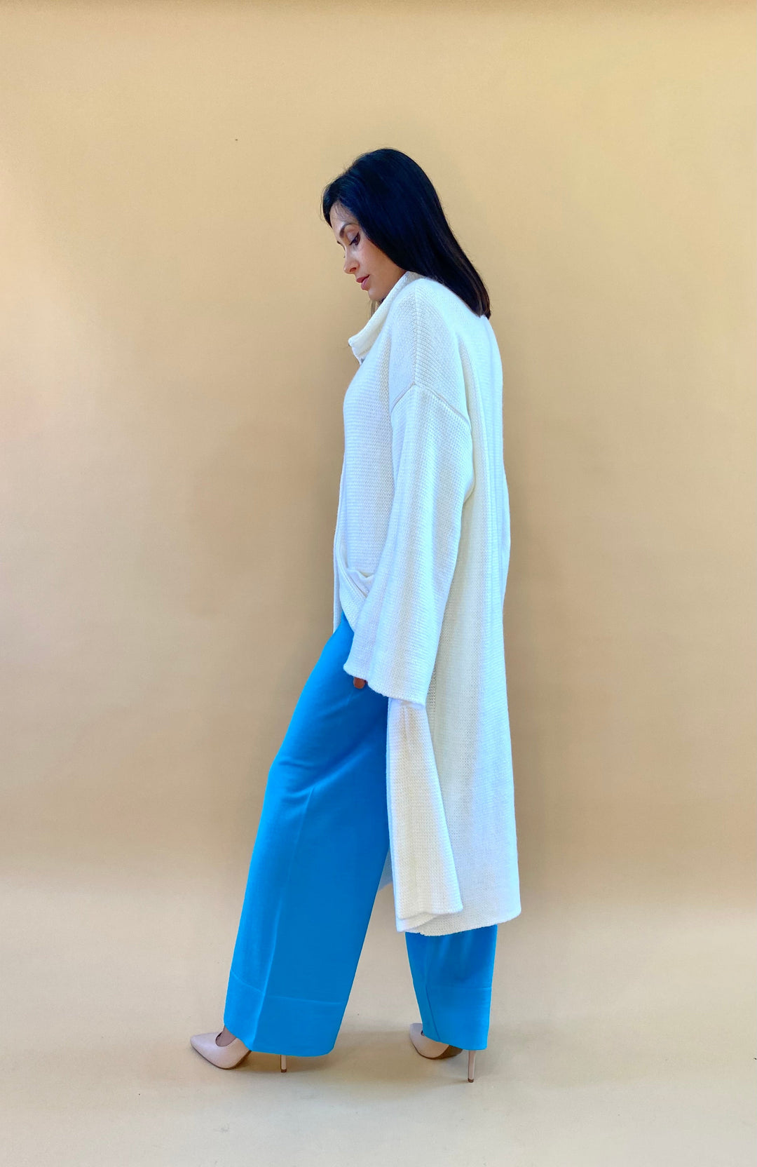 Woman in a cream oversized cardigan and blue pants against a beige background