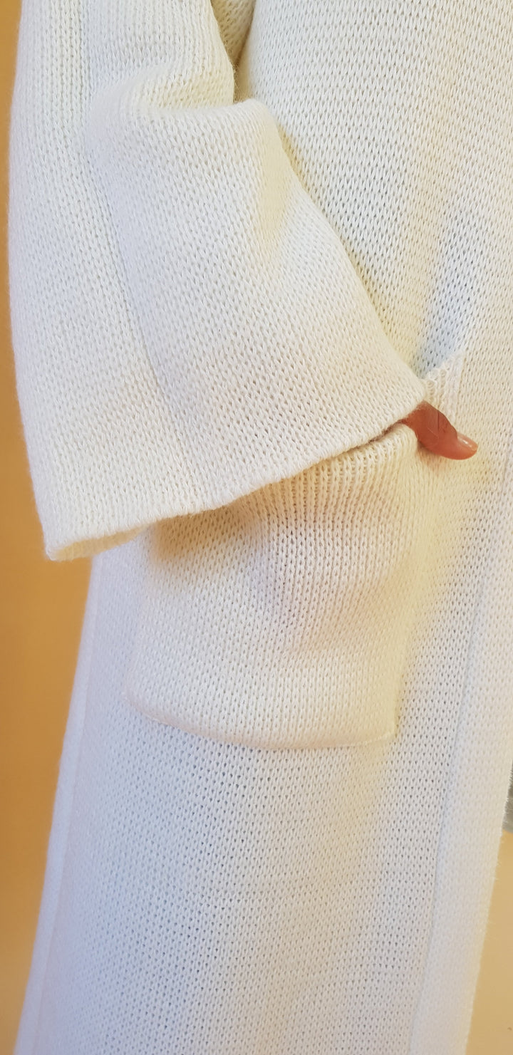 Close-up of a person reaching into the pocket of a cream-colored knit sweater