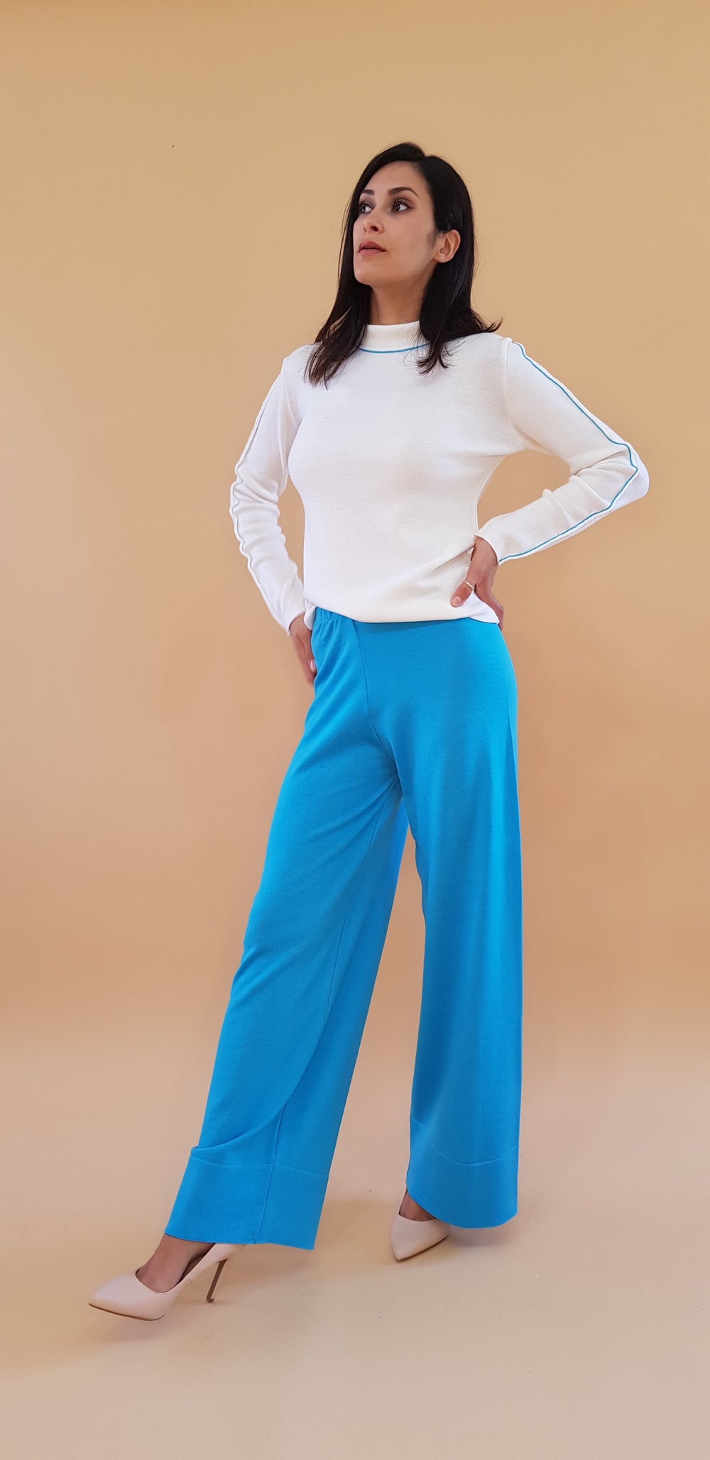 Woman wearing a white sweater and blue wide-leg pants against a beige background