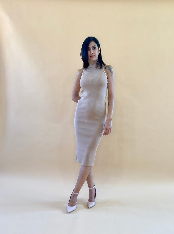 Woman in a beige sleeveless dress standing against a light brown background