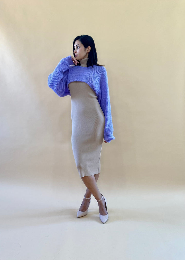 Woman posing in beige dress with oversized purple sweater against beige background