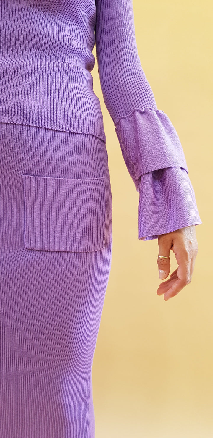 Person wearing a stylish purple ribbed outfit with large bell sleeves against a yellow background