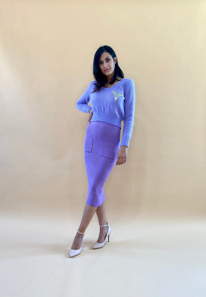 Woman wearing a lavender sweater and skirt set with high heels against beige background