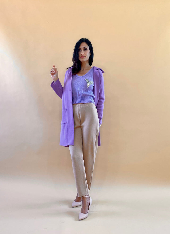 Woman wearing lilac coat and beige pants against a beige background