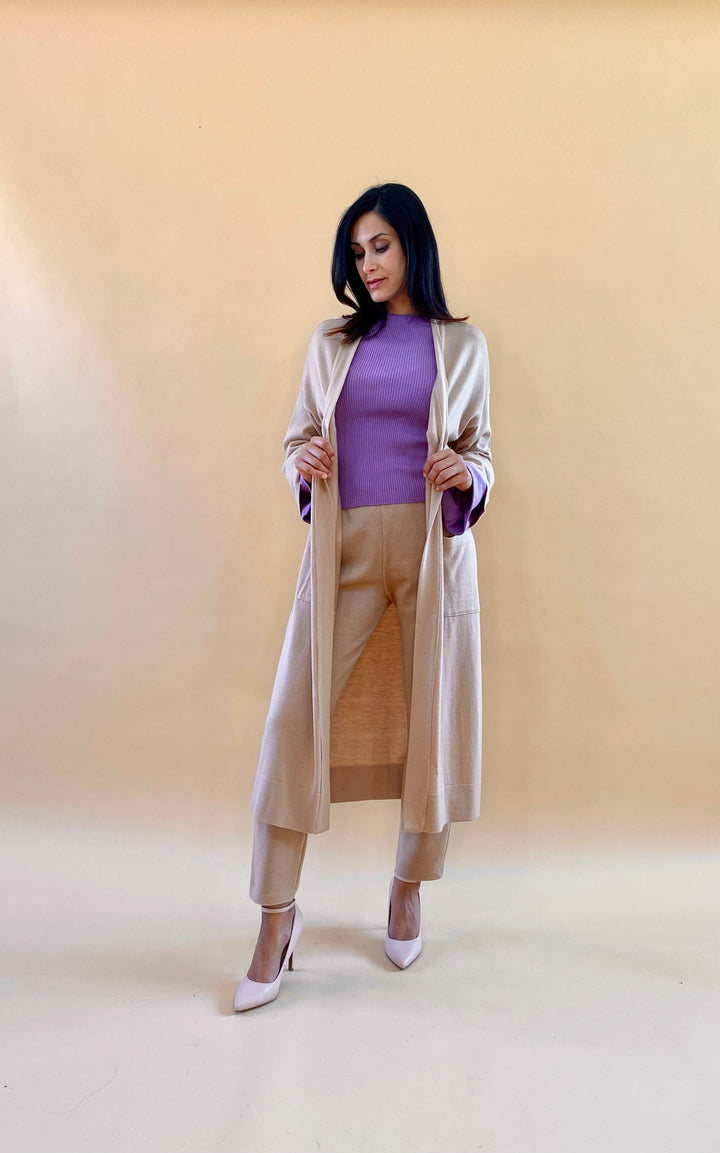 Woman in stylish beige outfit with purple top standing against beige background