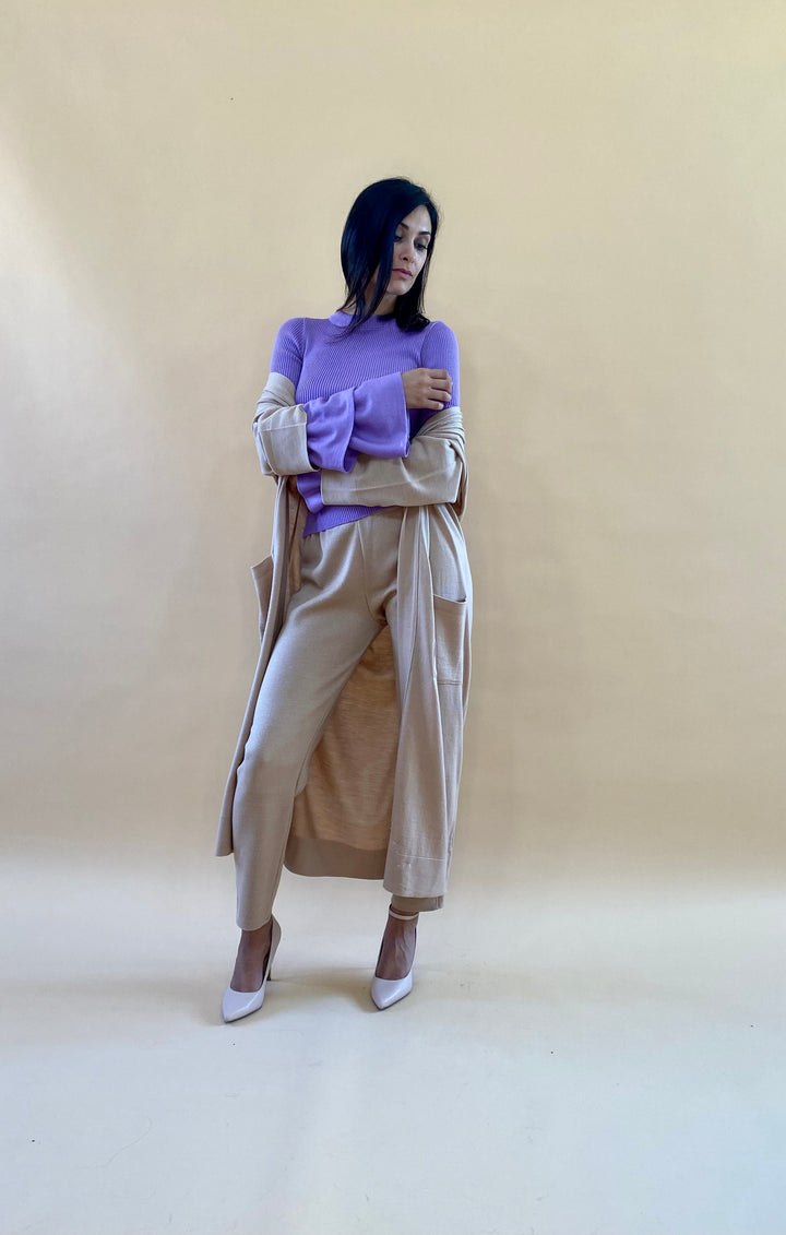 Woman in stylish beige and purple outfit posing against a neutral background